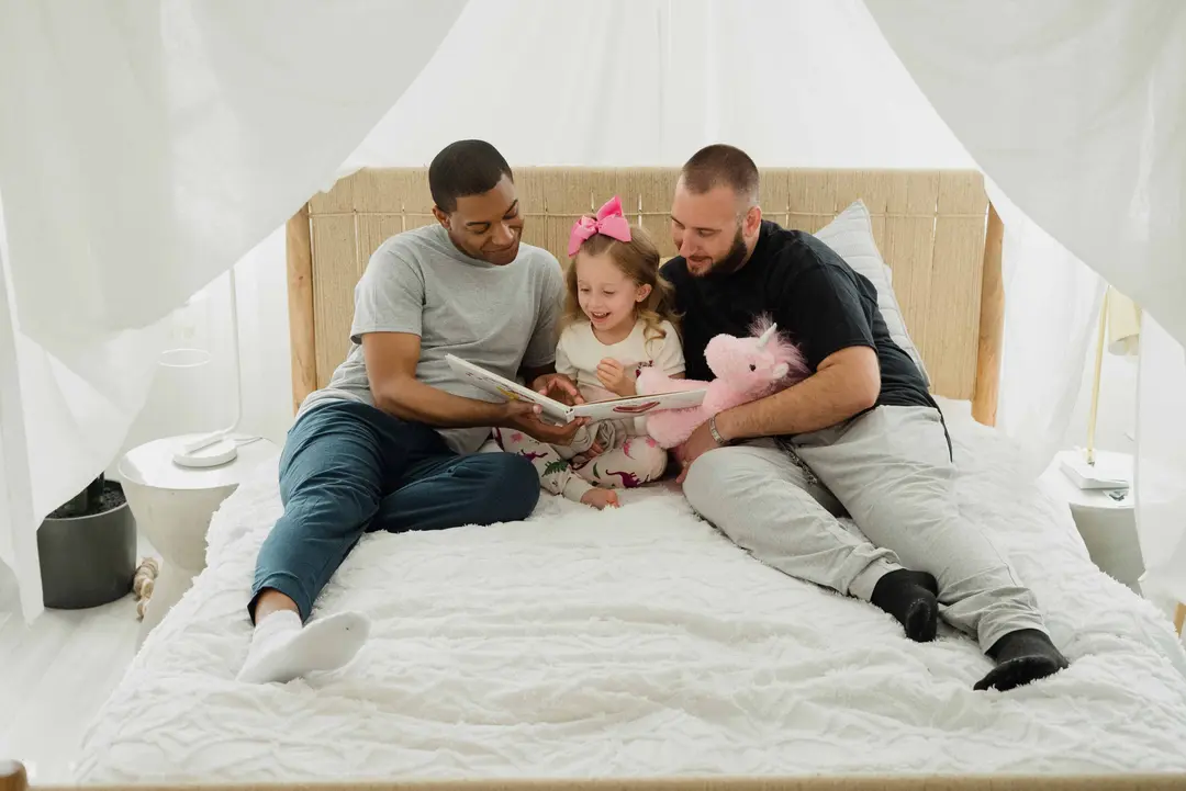 Kid reading a book in bed with parents